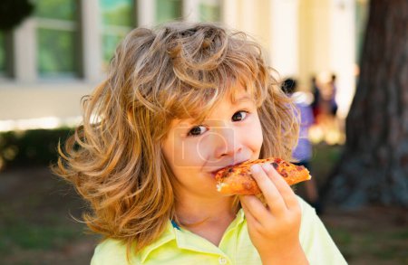 Téléchargez les photos : Un gamin qui mange une pizza. Le gamin mange une part de pizza pepperoni. Les enfants adorent la pizza - en image libre de droit