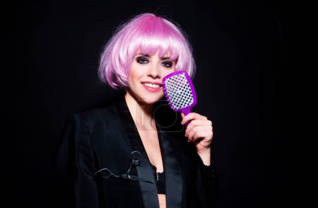 Foto de Retrato de encantadora mujer de moda divertida con peluca rosa peinando el cabello con peine de cepillo, aislado - Imagen libre de derechos