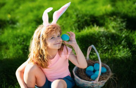 Foto de Niño cazando huevos de Pascua. Niño con huevos de Pascua y orejas de conejo al aire libre. - Imagen libre de derechos