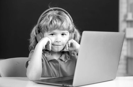 Photo for Clever school boy, cute pupil wears headphones writing on laptop, listen audio lesson use computer. Elementary school and education - Royalty Free Image