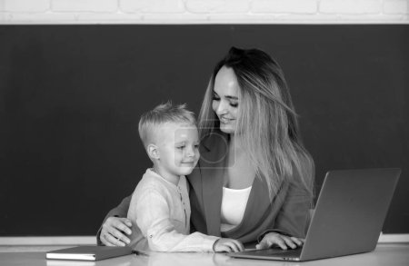 Photo for Little school child son using laptop with mother. Elementary school classroom. Teacher and schoolchild pupil in class. Mother and son together using computer laptop - Royalty Free Image
