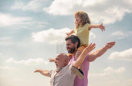Men generation: grandfather father and grandson playing with raising hands or open arms outdoor on sky. Boy dreams of becoming a pilot. Start, creativity startup concept