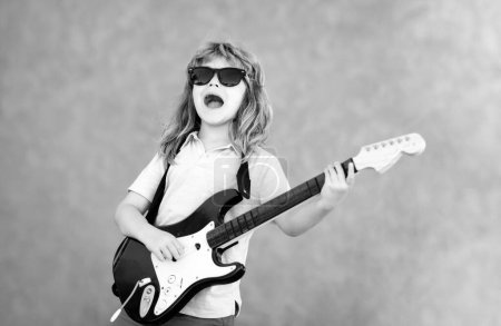 Foto de Funny rock child with guitar. Little boy in sunglasses. Kids music concept. Rock and roll guitar. Boy guitarist - Imagen libre de derechos