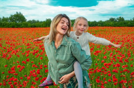 Photo for Mother and daughter walking through a flowering poppy field. Child and mom piggyback ride on summer poppies meadow with poppys flowers. Happy motherhood. Spring design - Royalty Free Image