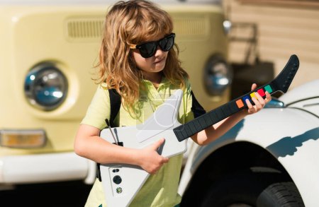 Foto de Retrato de un niño divertido con gafas practicando una canción durante una lección de guitarra en la calle. Concepto musical, escuela de música para niños. Concierto de rock. Niño músico guitarrista tocando la guitarra eléctrica - Imagen libre de derechos
