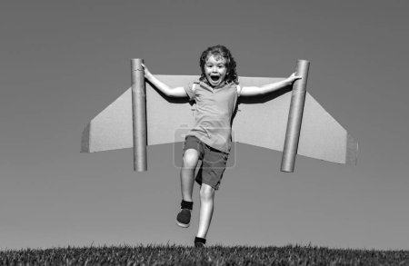 Téléchargez les photos : Joyeux enfant jouant dans le parc. Enfant s'amuser avec des ailes de papier jouet. Petit garçon rêvant de devenir pilote. Enfant drôle sur un fond bleu ciel avec espace de copie - en image libre de droit
