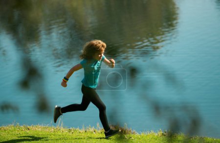 Téléchargez les photos : Les enfants font du jogging dans le parc extérieur. Activité sportive saine pour les enfants. Petit garçon à la compétition d'athlétisme. Jeune athlète en entraînement. Exercice du coureur. Enfants courant sur la prairie verte contre la mer ou - en image libre de droit