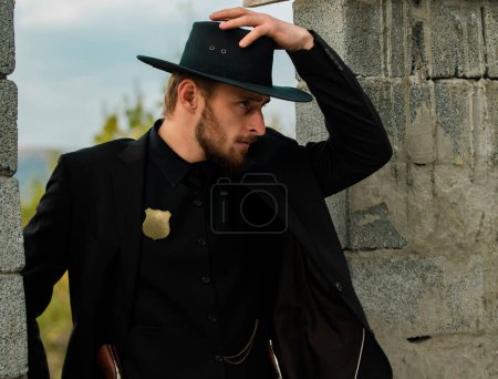 Sheriff or cowboy in black suit and cowboy hat. Man with west vintage pistol revolver gun. American western, sheriff