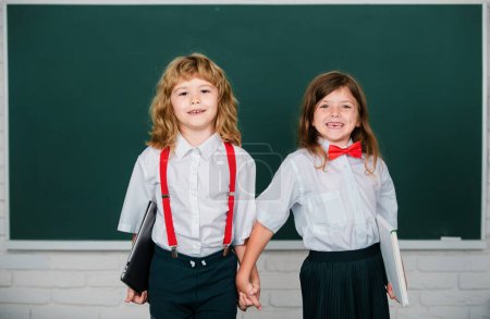 Photo for Happy girl and boy school friends. Face portrait of two schoolkids. Children couple at primary school classmates, young students. School friends holding hand near blackboard - Royalty Free Image