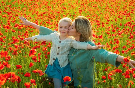 Foto de Happy spring family. Carefree mom with a child girl in a field of red poppies enjoys nature. Mother and little daughter in the poppy field. A young woman with her daughter in in a poppy field - Imagen libre de derechos