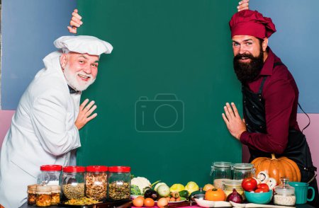 Foto de Chef cocinero mostrando en el tablero en blanco. Dos chefs masculinos sonrientes, cocineros o panaderos con menú en blanco. Cocinero - Imagen libre de derechos