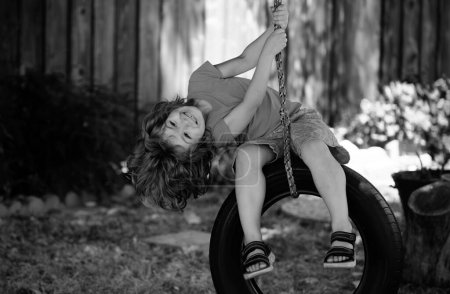 Téléchargez les photos : Drôle garçon enfant avoir amusant avec chaîne balançoire sur aire de jeux en plein air - en image libre de droit