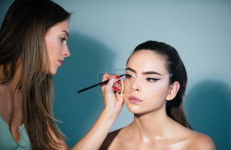 Photo for Makeup artist applies eye shadow. Hand of visagiste, painting cosmetics of young beauty model girl. Fashion shiny highlighter on skin. Professional make up process - Royalty Free Image