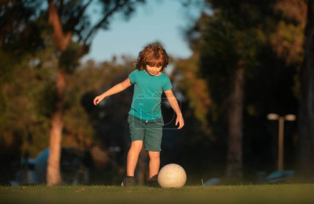 Foto de Niño jugador de fútbol pateando fútbol en el campo de deportes. Niños activos. Niño jugador de fútbol en el parque - Imagen libre de derechos