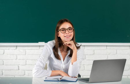 Foto de Retrato de una joven universitaria en gafas que estudia en el aula en el portátil en clase con fondo de pizarra - Imagen libre de derechos