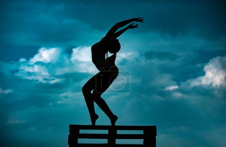 Photo for Silhouette of woman stretching. Young girl practicing yoga, doing fit exercise, working out. Dance studio. Cloudy sky background - Royalty Free Image