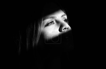 Téléchargez les photos : Portrait of elegant woman with light on a black background. Beautiful female face in the darkness - en image libre de droit