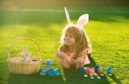 Téléchargez les photos : Enfant garçon avec oeufs de Pâques et oreilles de lapin en plein air. Drôle de garçon, lapin de Pâques enfants - en image libre de droit