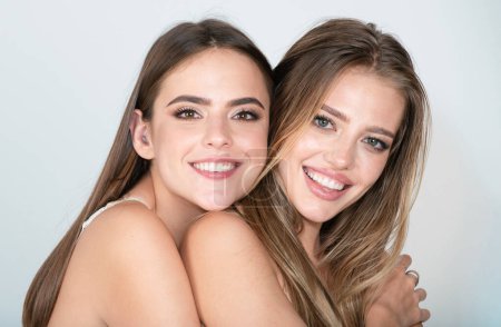 Foto de Women face of two happy smiling sexy girls, close-up. Beauty portrait of young happy beautiful blonde and brunette women. Two women friends laughing with a perfect white teet - Imagen libre de derechos