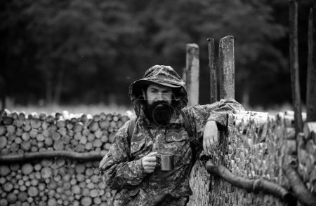 Téléchargez les photos : Portrait d'un voyageur buvant du thé ou du café chaud avec tasse en émail, tasse en métal. Voyage style de vie campagne et concept d'aventure. L'homme à la nature - en image libre de droit