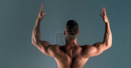 Foto de Modelo de fitness. Un tipo con una figura atlética, con un torso desnudo. Hombre musculoso de vuelta en el fondo gris. Modelo de ajuste masculino fuerte - Imagen libre de derechos