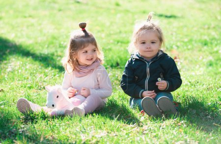 Photo for Cute boy and girl sit on grass on summer field. Baby child in green grass on spring lawn. Little kids walking in the park - Royalty Free Image