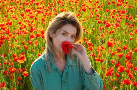 Foto de Mujer en el prado de amapolas. Hermosa chica en un campo de amapola al aire libre. Flores de amapolas cerca de la boca - Imagen libre de derechos