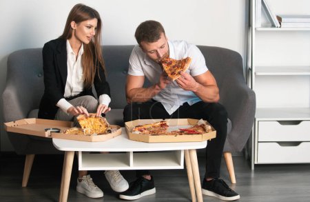 Téléchargez les photos : Homme d'affaires et femme d'affaires en pause déjeuner au bureau, mangeant une part de pizza. Des gens heureux déjeunent au bureau de coworking pendant la pause - en image libre de droit