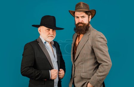 Head shot portrait of elderly mature senior dad and grownup son. Two male generations family. Men in hat. Men in different ages in studio