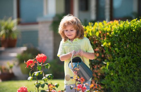 Foto de Un niño derramando agua sobre los árboles. El niño ayuda a cuidar las plantas en el jardín. Niño pequeño con una regadera en el patio trasero - Imagen libre de derechos
