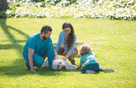 Téléchargez les photos : Famille emmenant chien pour une promenade à la campagne. Portrait extérieur de la famille heureuse dans le parc d'été, jeune couple avec enfant garçon sur l'herbe - en image libre de droit