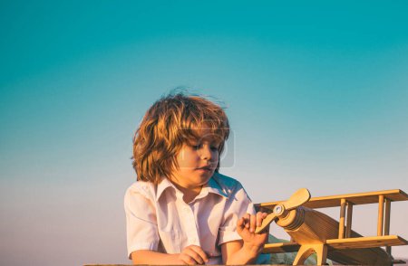 Téléchargez les photos : Enfant garçon jouant avec un avion jouet en bois, rêve de devenir pilote. Rêves d'enfants. Enfant pilote aviateur avec avion en bois - en image libre de droit