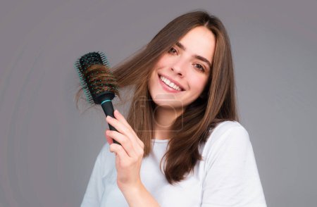 Téléchargez les photos : Fille souriante peigner les cheveux. Belle jeune femme tenant peigne cheveux lissés. Attrayant portrait de femme souriante avec peigne - en image libre de droit