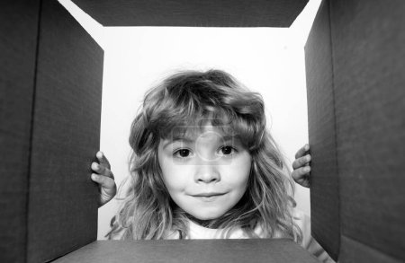 Téléchargez les photos : Enfant excité de 7 ans regardant dans la boîte, boîte en carton d'expédition. Emballage d'ouverture enfant - en image libre de droit