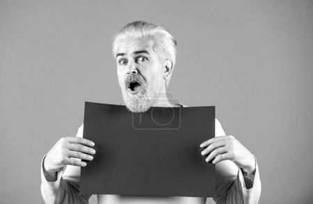 Foto de Feliz hombre de mediana edad presentando papel vacío. Modelo masculino sosteniendo tablero blanco. En blanco, papel vacío, cartelera con espacio de copia para el texto - Imagen libre de derechos
