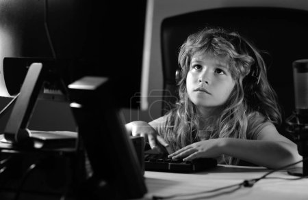 Téléchargez les photos : Un petit garçon utilise un bureau la nuit, un enfant avec écran d'ordinateur dans la chambre avec de la foudre au néon. École, étude, concept d'apprentissage en ligne - en image libre de droit