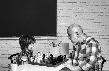 Foto de Grandfather and grandson boy playing chess, men generation. Different ages, grandfather and child grandson study chess together in home classroom - Imagen libre de derechos