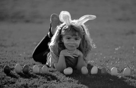 Photo for Kids boy hunting easter eggs. Child boy with easter eggs and bunny ears on grass - Royalty Free Image