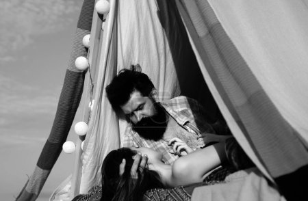 Téléchargez les photos : Couple romantique en tente camping sur fond de nature. Aventure pour les jeunes amis le jour d'été. Couple hipster tendre baisers dans la tente du camp - en image libre de droit