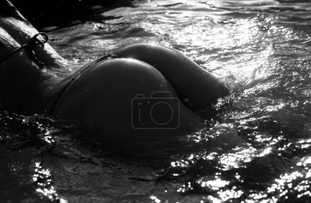 Téléchargez les photos : Sensual bum in swimming pool close-up, summer journey, woman with hot natural butt relax in water. Wet body, backside in sexy bikini. Seduction and pleasure model. Luxury passion buttocks - en image libre de droit