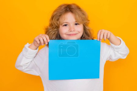 Foto de Niño feliz con hoja de papel, aislado sobre fondo amarillo. Retrato de un niño sosteniendo un cartel en blanco, póster. Tablero vacío para plantillas banner, spase de copia, maqueta - Imagen libre de derechos