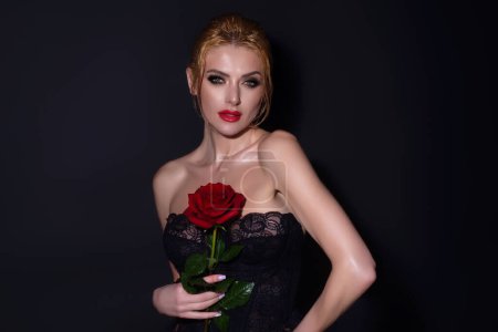 Foto de Retrato de estudio de belleza. Hermoso modelo con flor de rosa roja, aislado sobre fondo de estudio negro. Encantadora joven con maquillaje perfecto - Imagen libre de derechos