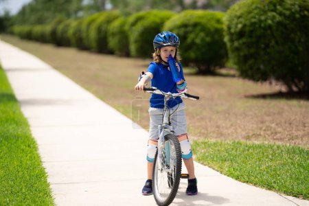 Child riding bicycle. Little kid boy in helmet on bicycle along bikeway. Happy cute little boy riding bicycle in summer park. Child in protective helmet for bike cycling on bicycle. Kid riding bike