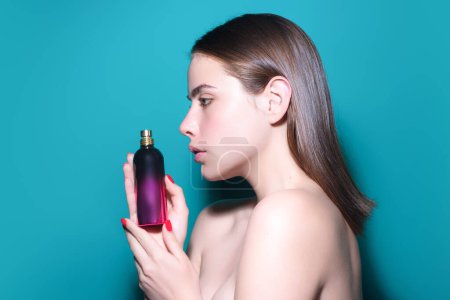 Photo for Female perfume. Girl with perfume, young beautiful woman holding bottle of perfume and smelling aroma. Sensual young woman holding perfume. Woman holding a perfumes bottle. Perfumes fragrance - Royalty Free Image
