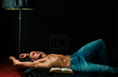 Foto de Vida de lujo. Sin camisa musculoso culturista hombre leyendo libro, acostado en la cama - Imagen libre de derechos