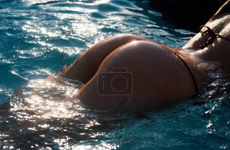 Téléchargez les photos : Sensual ass in swimming pool close up, summer journey, woman with hot natural butt relax in water. Wet body, backside in sexy bikini. Seduction and pleasure model. Luxury passion buttocks - en image libre de droit