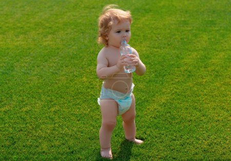 Photo for Baby drinking water outdoor on green grass. Healthy child - Royalty Free Image