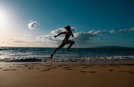 Téléchargez les photos : Femme coureuse sur la plage. Femme courant au coucher du soleil sur la plage. Sport d'été et concept de liberté. Entraînement des athlètes au crépuscule - en image libre de droit