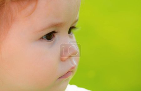 Photo for Cute baby face closeup on green grass in summertime. Funny little kid close up portrait on green nature - Royalty Free Image