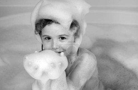 Foto de Niños bañándose. Niño divirtiéndose en el baño con burbujas. Niño feliz disfrutando del baño. Niño sonriendo en el baño con espuma de jabón. El niño se baña en un baño con espuma - Imagen libre de derechos